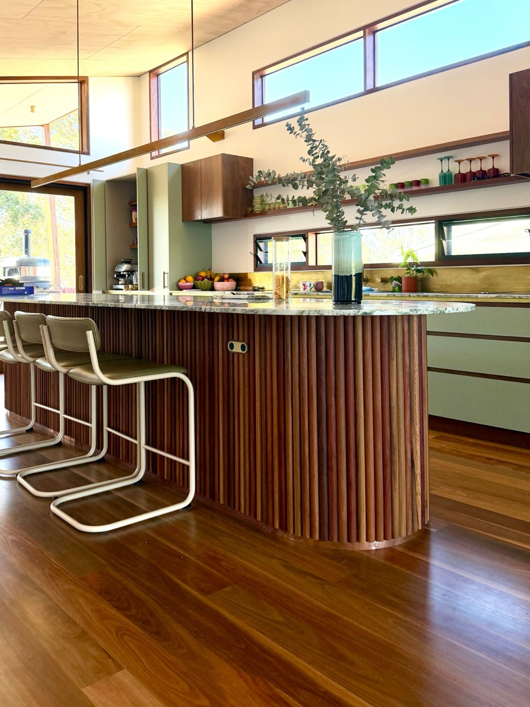 Kitchen island wrapped in vertical timber dowels, with a stone top and bar stools