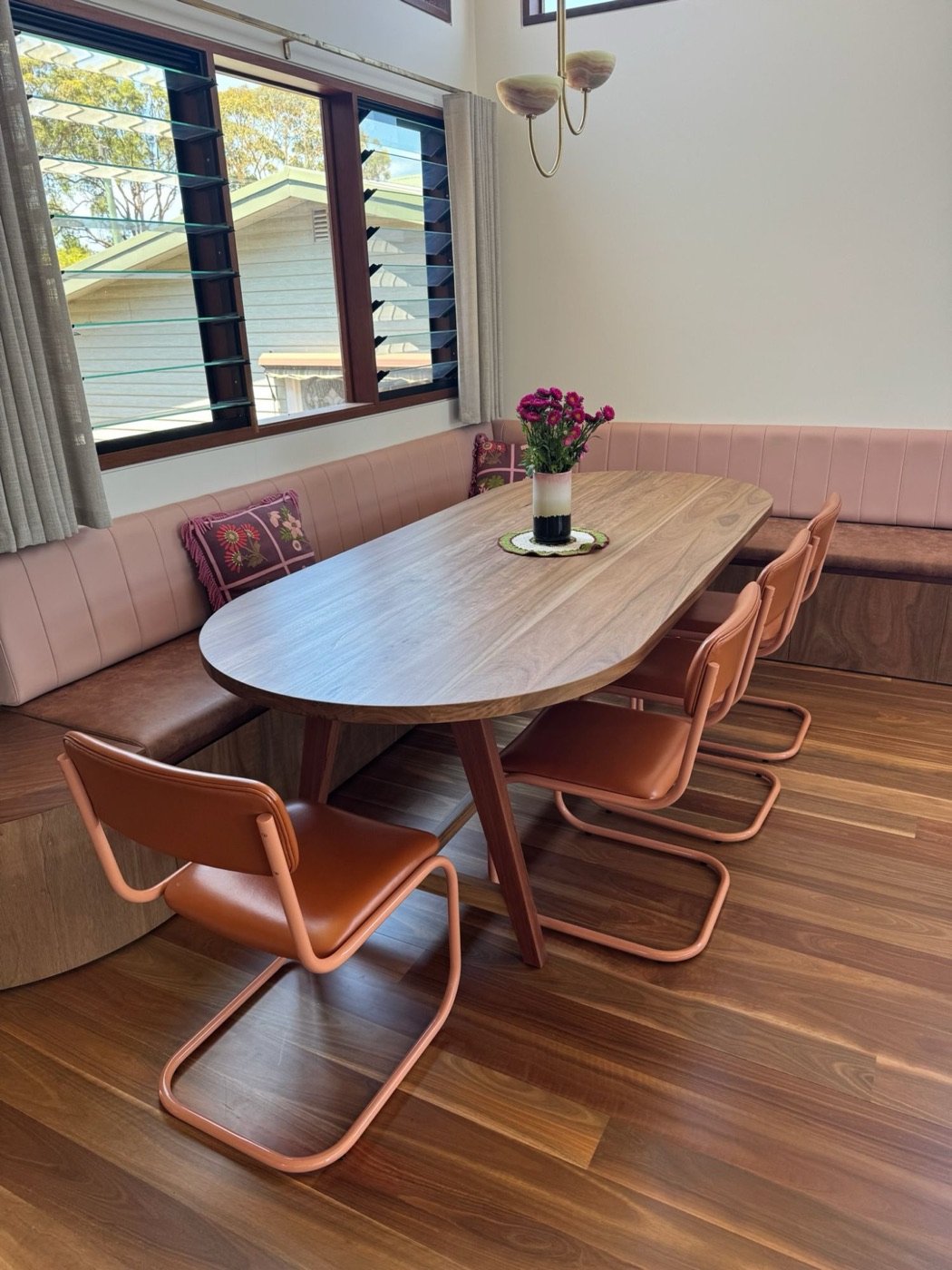Oval timber dining table beside built-in banquette seating