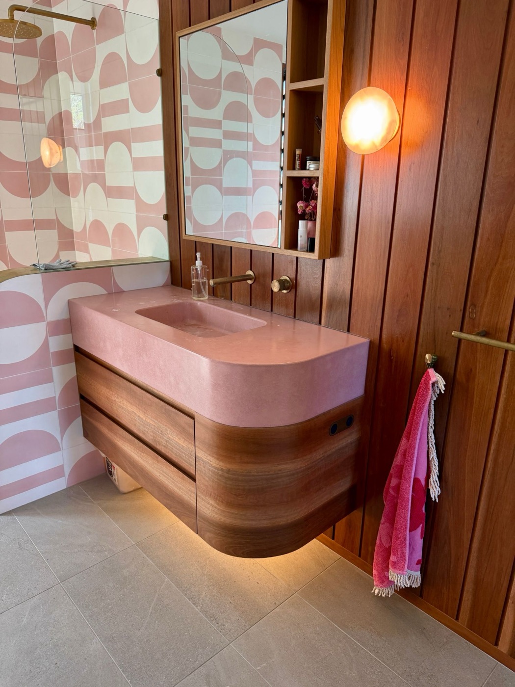 Floating curved timber vanity under a pink basin